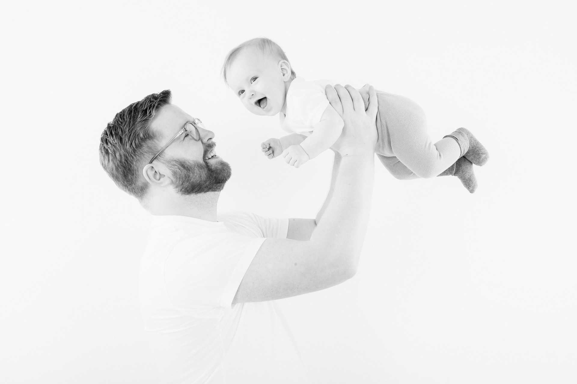 Far løfter grinende baby op i luften i professionelt studie