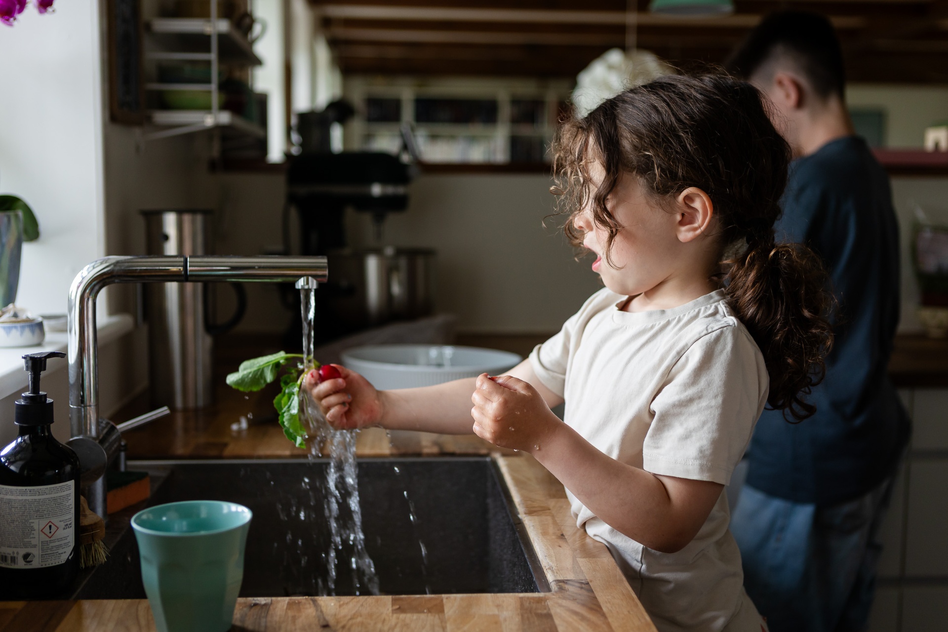 Barn vasker grøntsager i køkkenet under livsstilsfotografering i hjemmet