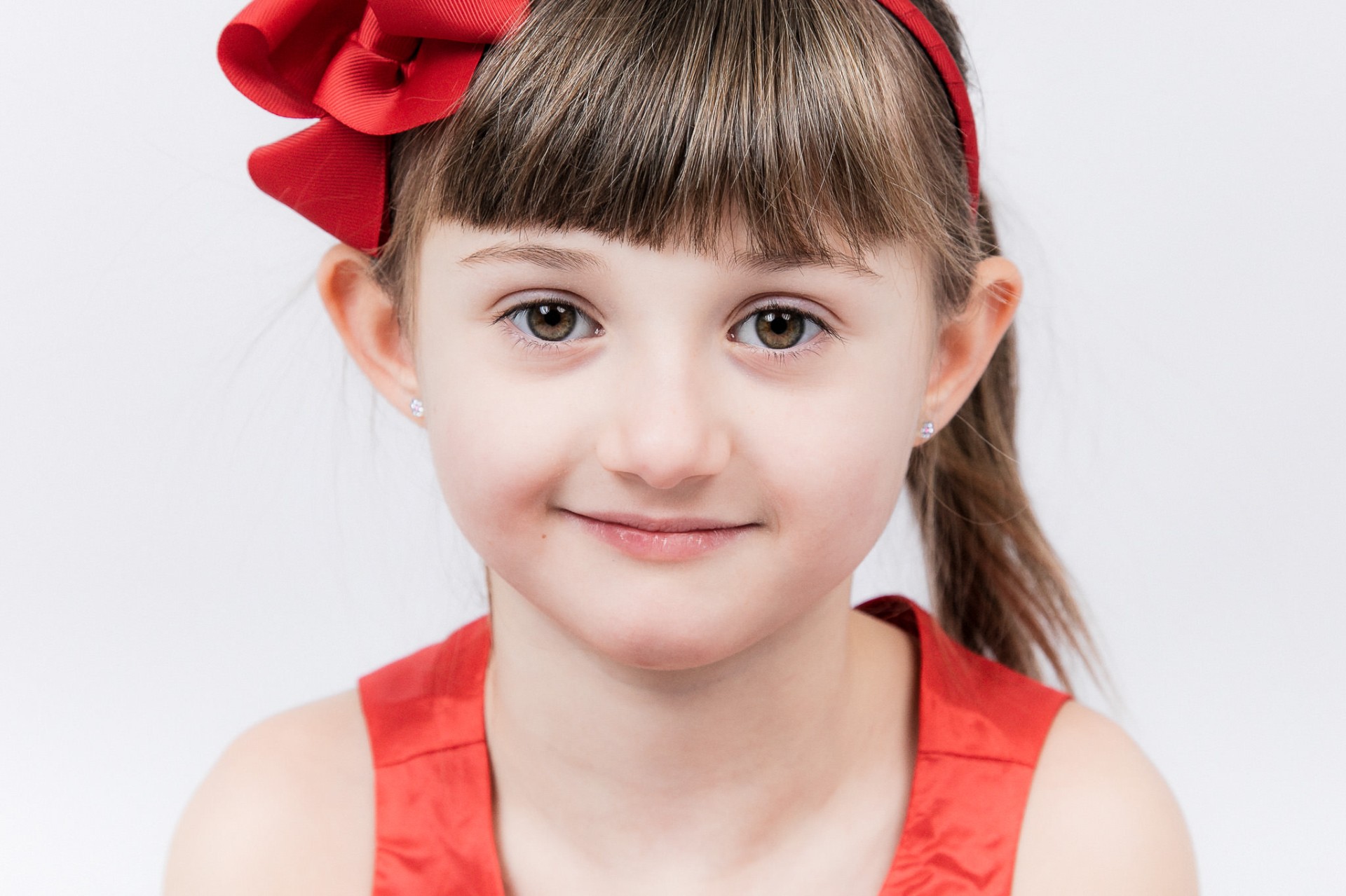 Pige med rød sløjfe smiler i professionelt studie-portræt